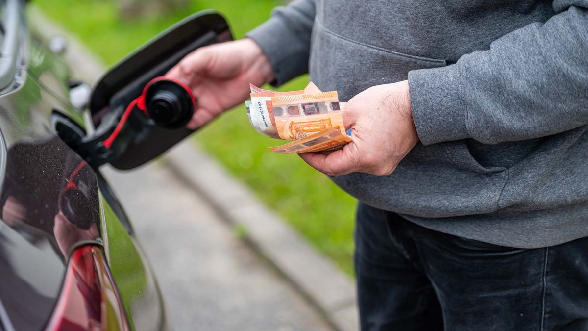 un hombre reposta gasolina mientras sostiene billetes y monedas de euro