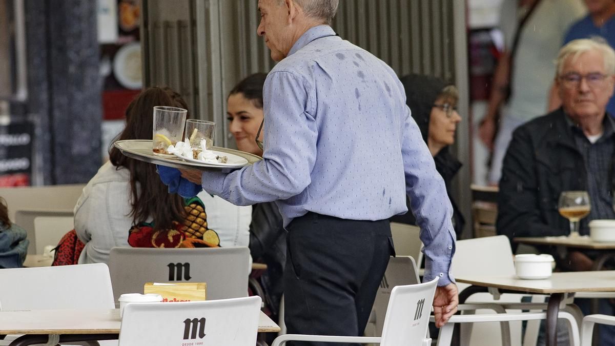 Un camarero lleva una bandeja a una de las mesas.