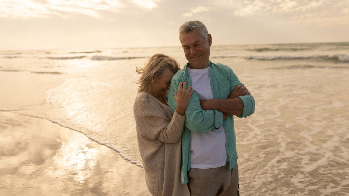 Dos personas mayores sonríen en la playa.