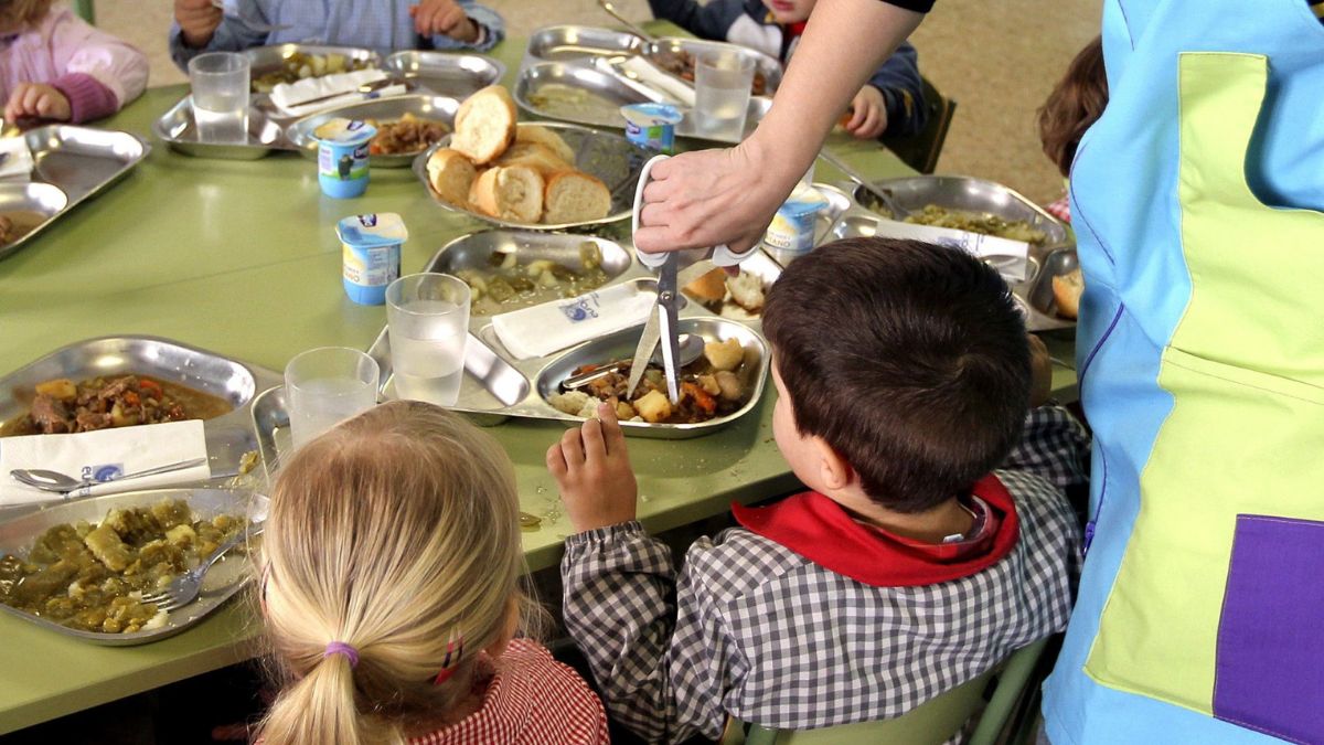 Una monitora de comedor parte la carne a un niño