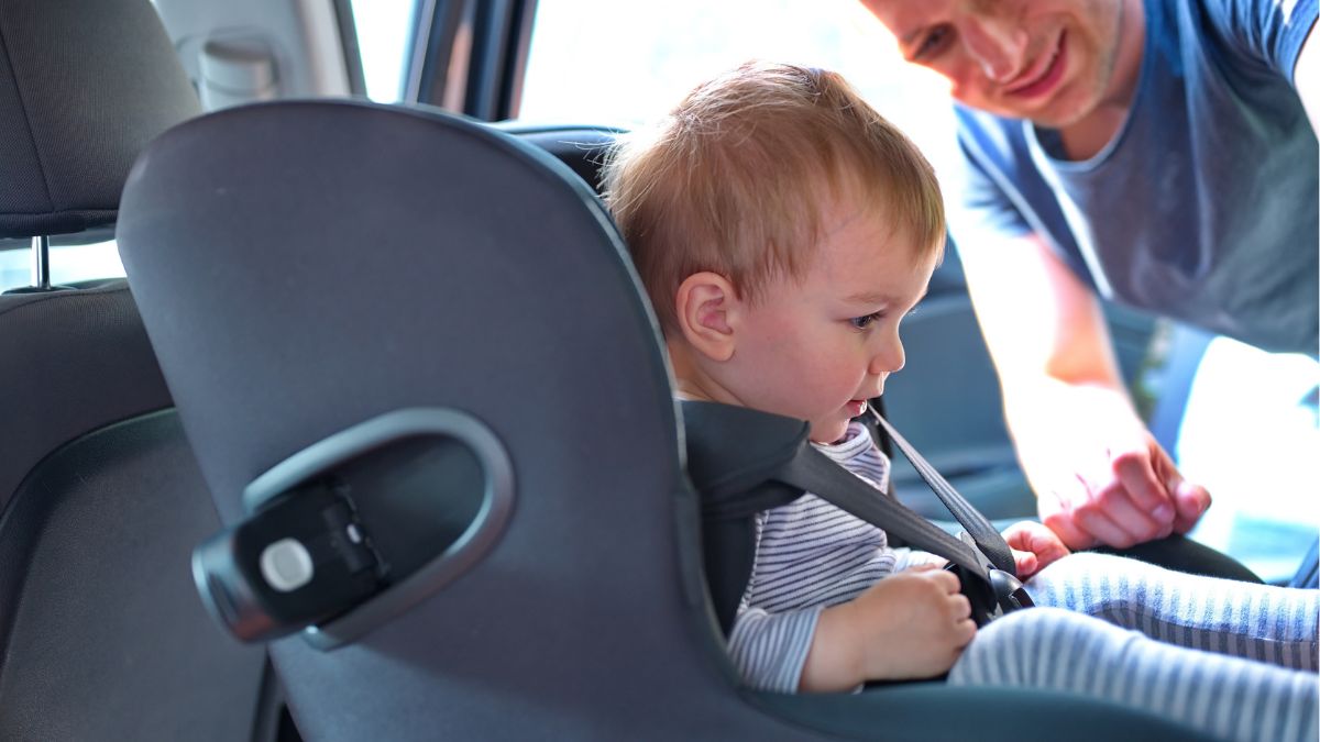 Un padre sienta a un niño en una silla de coche.