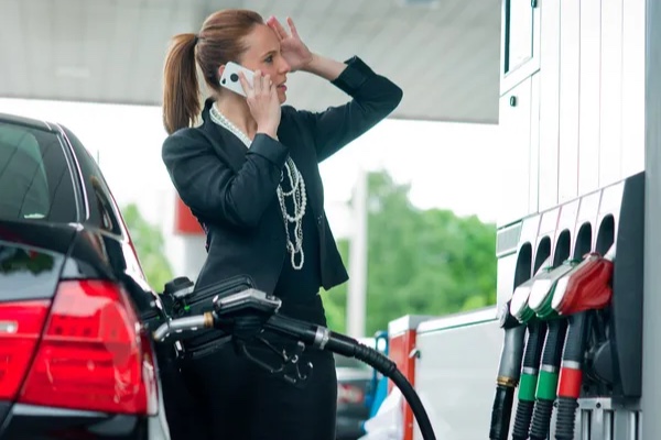 Mujer hablando por teléfono móvil mientras echa gasolina
