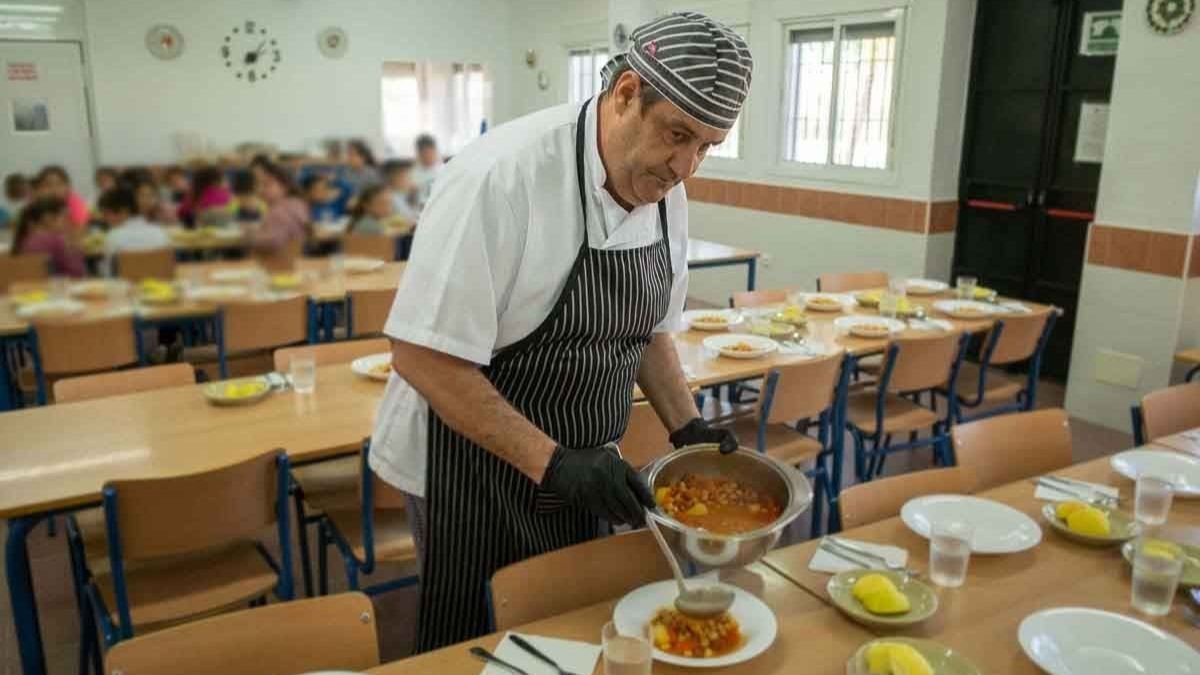 Un cocinero prepara platos en un comedor escolar.